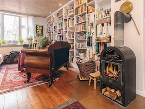 A cozy room with a wooden sofa, a fireplace, bookshelves, and a window.