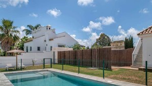Una piscina con agua cristalina azul, rodeada por un edificio blanco con techo de tejas y cerca de madera.
