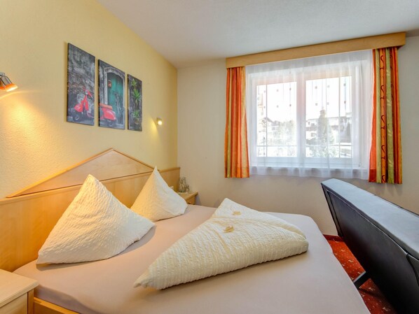Quarto de hotel com cama, escrivaninha e janela com cortinas.