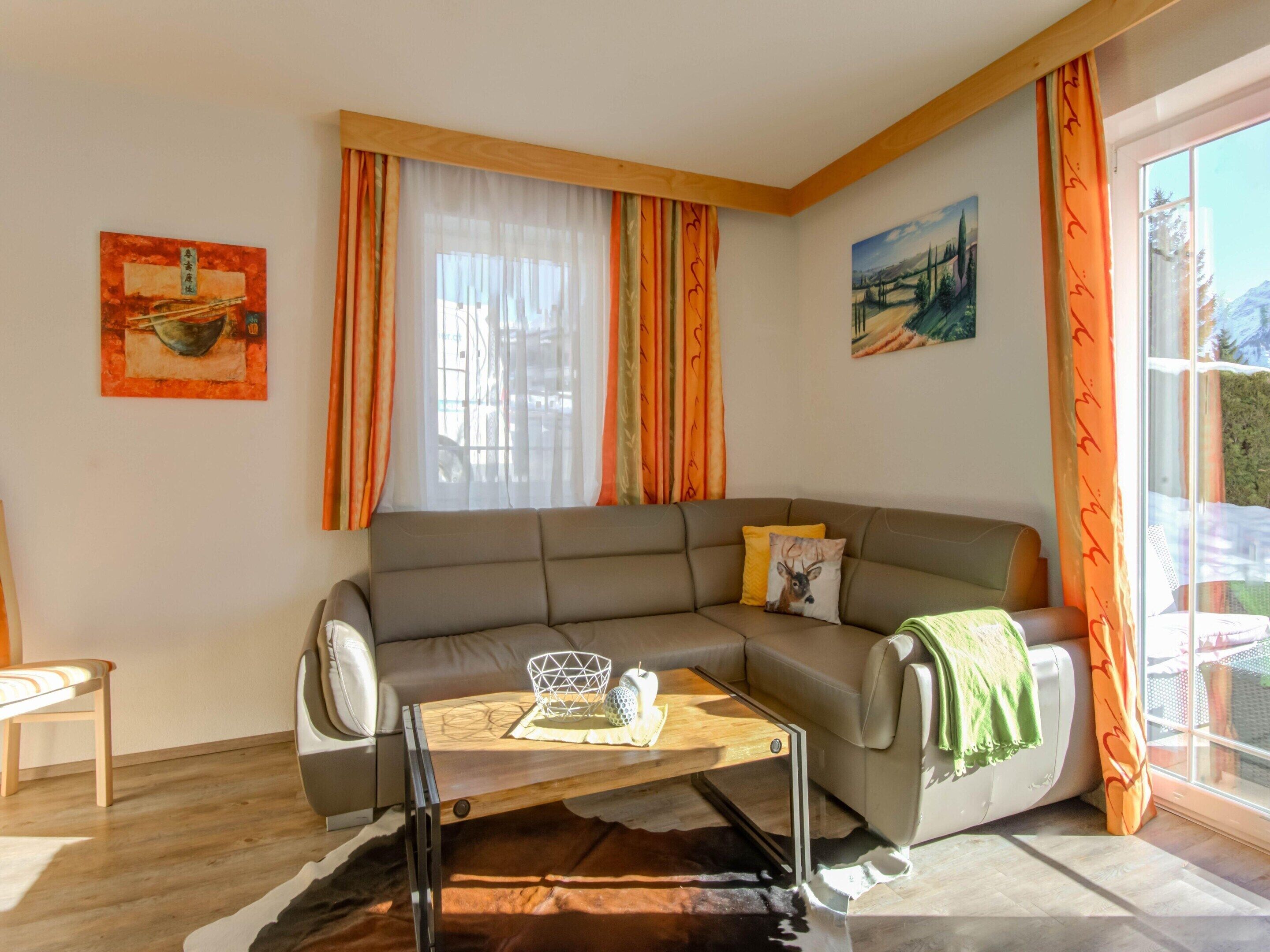 Un salon avec un canapé gris, une table basse en bois et une fenêtre ornée de rideaux orange.