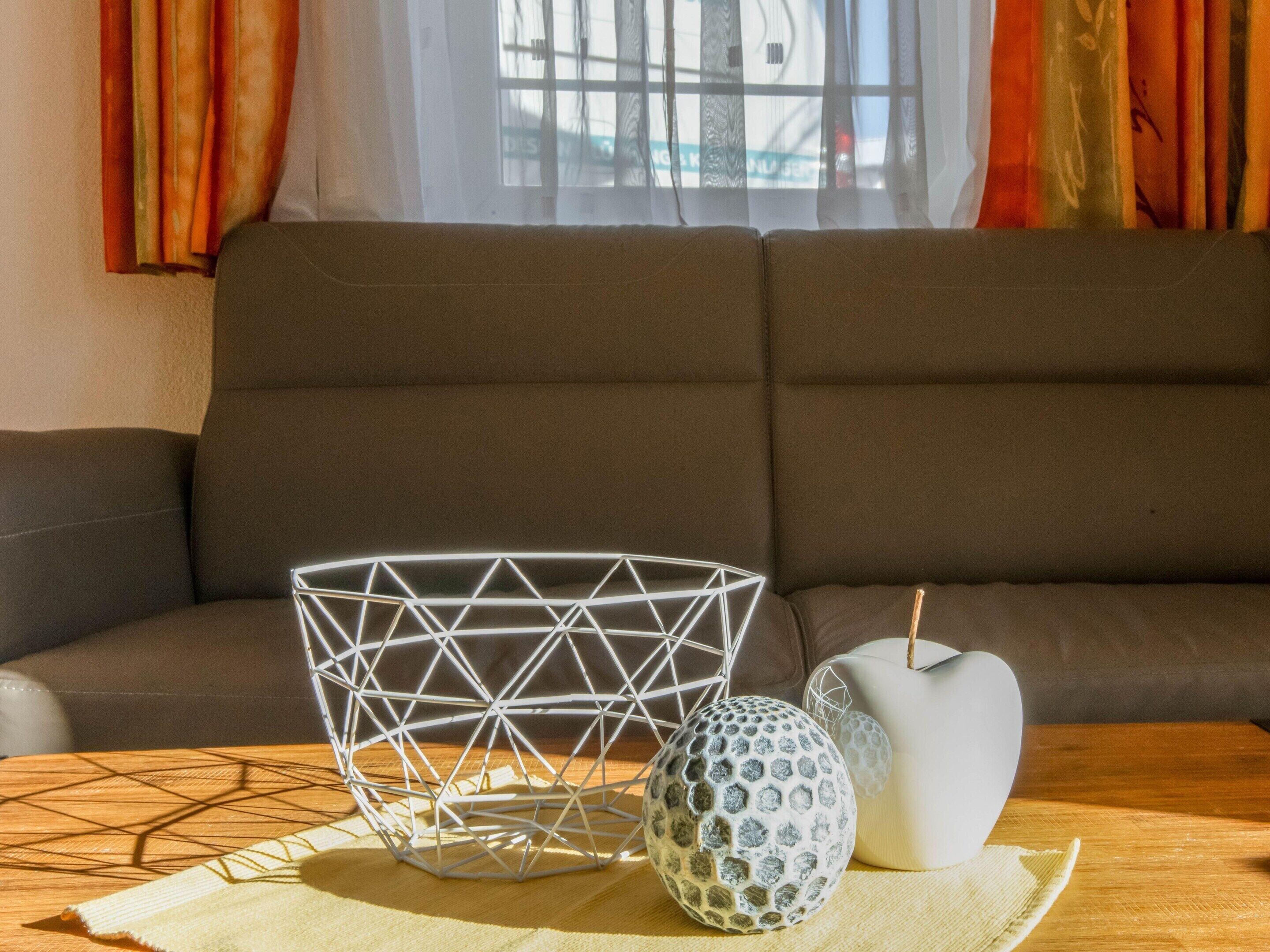 Una sala moderna con una cesta geométrica blanca, un florero blanco texturizado y una mesa de madera.