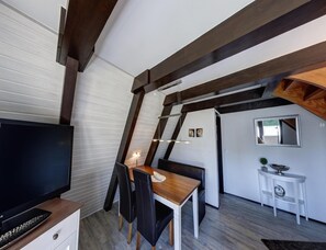 A modern interior with a TV, wooden dining table, black chairs, and a white side table. - Nurdachhaus in Burhave (Butjadingen)