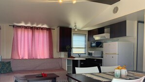 A compact living space with a sofa, dining table, chairs, kitchenette, and a window with curtains. - Comfortable Seaside Home in Conil (Vejer de la Frontera)