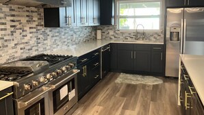 A modern kitchen with dark cabinetry, a stainless steel range, a built-in oven, a gas stove, a window with a view, and a water dispenser. - Open water 3bdrm 3bath home with dock for 20 foot boat along with pool & jacuzzi (St. Petersburg)