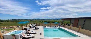 Una piscina en la azotea con sillas de descanso, sombrillas y un jacuzzi.