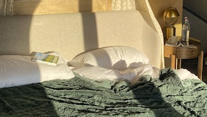 Une chambre à coucher avec un lit, une table de chevet, une lampe, une bouteille et une fenêtre avec des rideaux.
