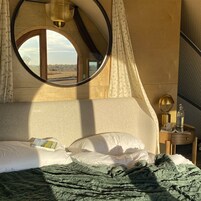 Un dormitorio con cama, una mesita de noche, lámpara, una botella y una ventana con cortinas.