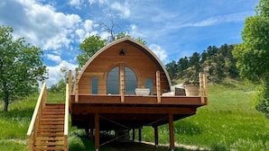 Une cabane en bois dotée d’un toit incurvé, d’un balcon et d’un escalier menant à l’entrée.