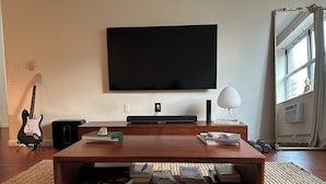 A living room with a flat-screen TV, a guitar, a lamp, and a coffee table with books. - Serene 2-bedroom apartment with AC in vibrant Bronx neighborhood (bronx)