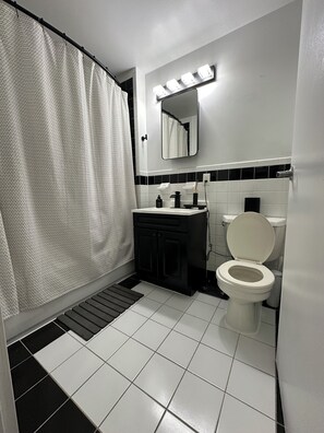 Een badkamer met douchegordijn, wastafel met spiegel erboven en toilet.