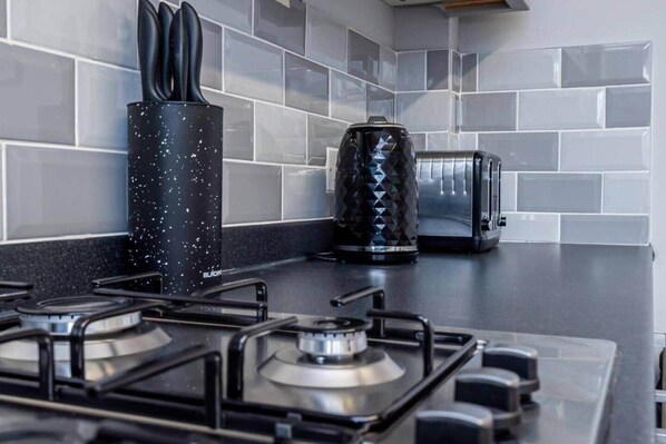 Una cocina con estufa a gas, un portalápices para cuchillos negros con motas, y un electrodoméstico negro con diseño de rombos.