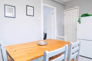 Un comedor con una mesa de madera y sillas blancas, una obra de arte en la pared y una puerta blanca con una planta.