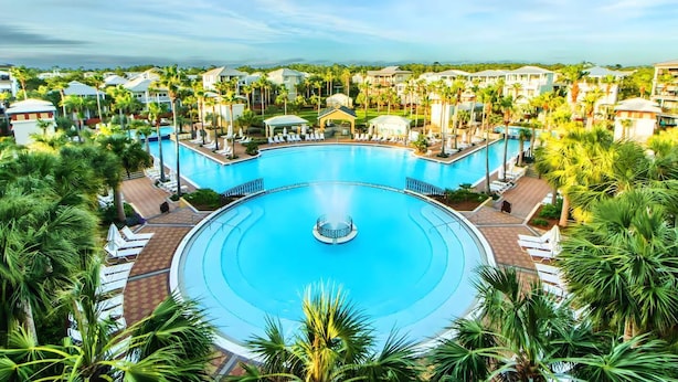 A large, circular swimming pool surrounded by palm trees and lounge chairs, with a view of resort buildings in the background. - Walk to Rosemary, Resort Pool, Bikes, Beach Gear (Panama City Beach)