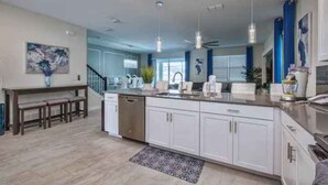 Una cocina moderna con armarios blancos, electrodomésticos de acero inoxidable e iluminación colgante.
