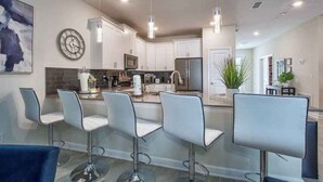Una cocina moderna con armarios blancos, electrodomésticos de acero inoxidable y una isla central con taburetes de bar.