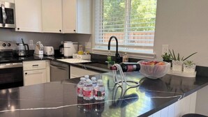 Una cucina moderna con mobili bianchi, un piano di lavoro nero, un forno a microonde in acciaio inossidabile, una macchina da caffè e un lavello.
