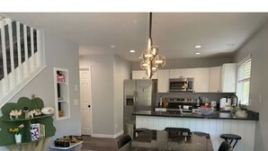 Una cucina moderna con mobili bianchi, un piano di lavoro nero e elettrodomestici in acciaio inossidabile. È presente un'area pranzo con un tavolo e sedie in marmo nero.