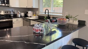 Una cucina moderna con mobili bianchi, un forno a microonde in acciaio inossidabile, una macchina per il caffè e un'ampia finestra.