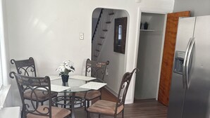 Ett modernt kök med ett kylskåp i rostfritt stål, ett matbord med fyra stolar och en trappa som leder till ett annat våningsplan.