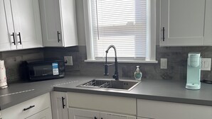Ett modernt kök med vita skåp, en diskho i rostfritt stål, en mikrovågsugn och en kaffemaskin från Keurig.