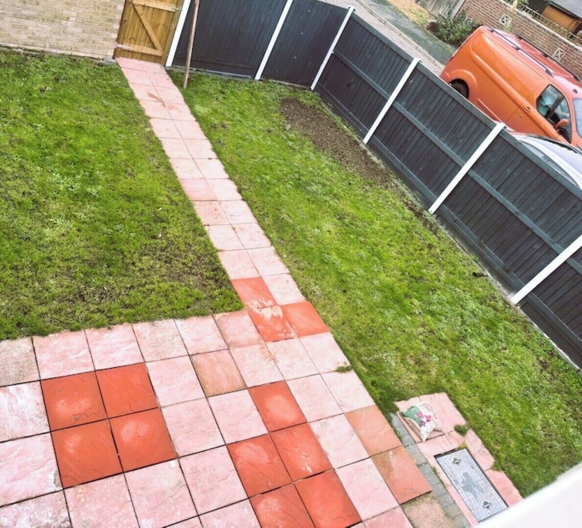 A backyard with a paved walkway, a grassy area, and a wooden fence.