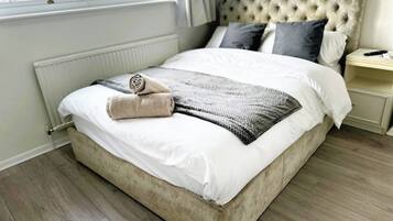 Un lit bien fait, avec une tête de lit beige, une serviette enroulée et une couverture grise.