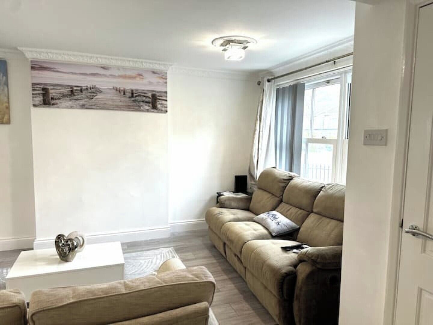A living room with a beige sofa, a white coffee table, and a painting on the wall.
