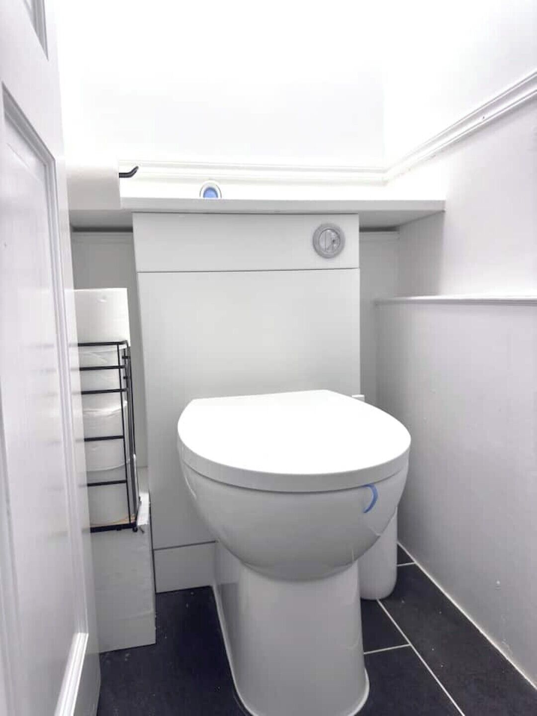 A small, white toilet in a narrow bathroom with a black floor.