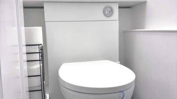 A small, white toilet in a narrow bathroom with a black floor.