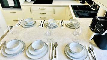 A dining table set with plates, glasses, and cutlery in a modern kitchen with a stove and oven in the background.
