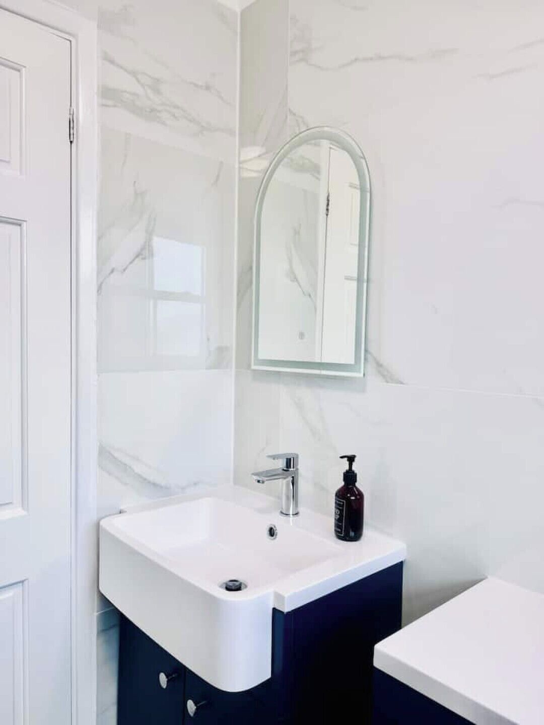 Een badkamer met een wit wastafelmeubel, donkere kastjes en een marmeren wand.