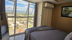 A bedroom with a large window, a bed, a desk, and an air conditioning unit. - Portmore Paradise: Pool & 24/7 Security (Portmore)