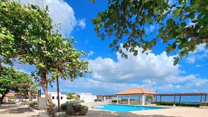 A pool area with a clear blue sky, a covered pavilion, and a view of the ocean. - Portmore Paradise: Pool & 24/7 Security (Portmore)