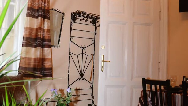 Ein Zimmer mit einer weißen Tür, einem Esstisch mit Stühlen, einem kleinen Tisch mit einem roten Topf und einer Pflanze sowie einem gestreiften Vorhang.
