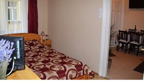 Ein Zimmer mit einem Bett, einem Nachttisch mit Lampe, einem an der Wand befestigten Fernseher und einer Essecke mit Stühlen und Tisch.
