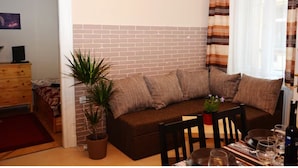 Ein Wohnzimmer mit einer Couch, einem Esstisch und einer Topfpflanze.