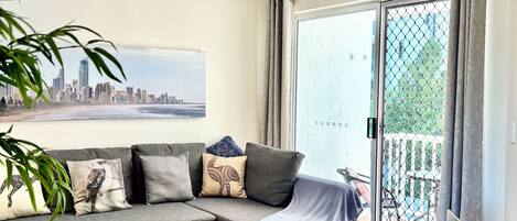 A modern living room with a grey sectional sofa, a cityscape painting, and a wooden floor.