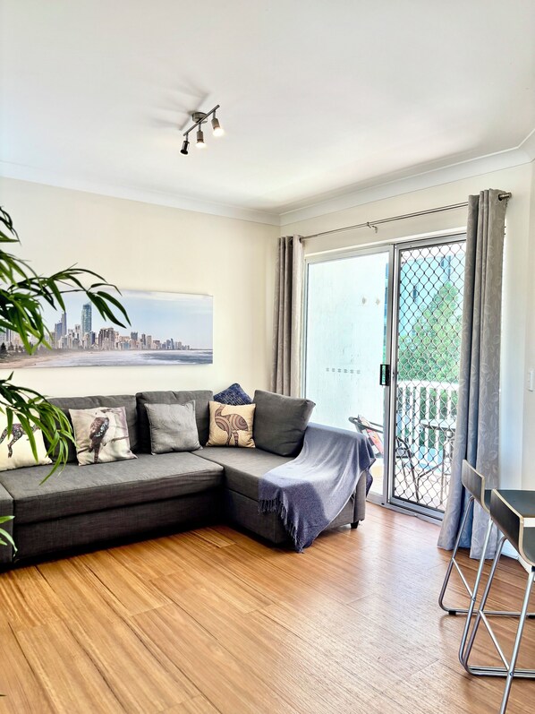 A modern living room with a grey sectional sofa, a cityscape painting, and a wooden floor. - Immaculate Fully Self Contained Apartment in Central Surfers Paradise (Surfers Paradise)