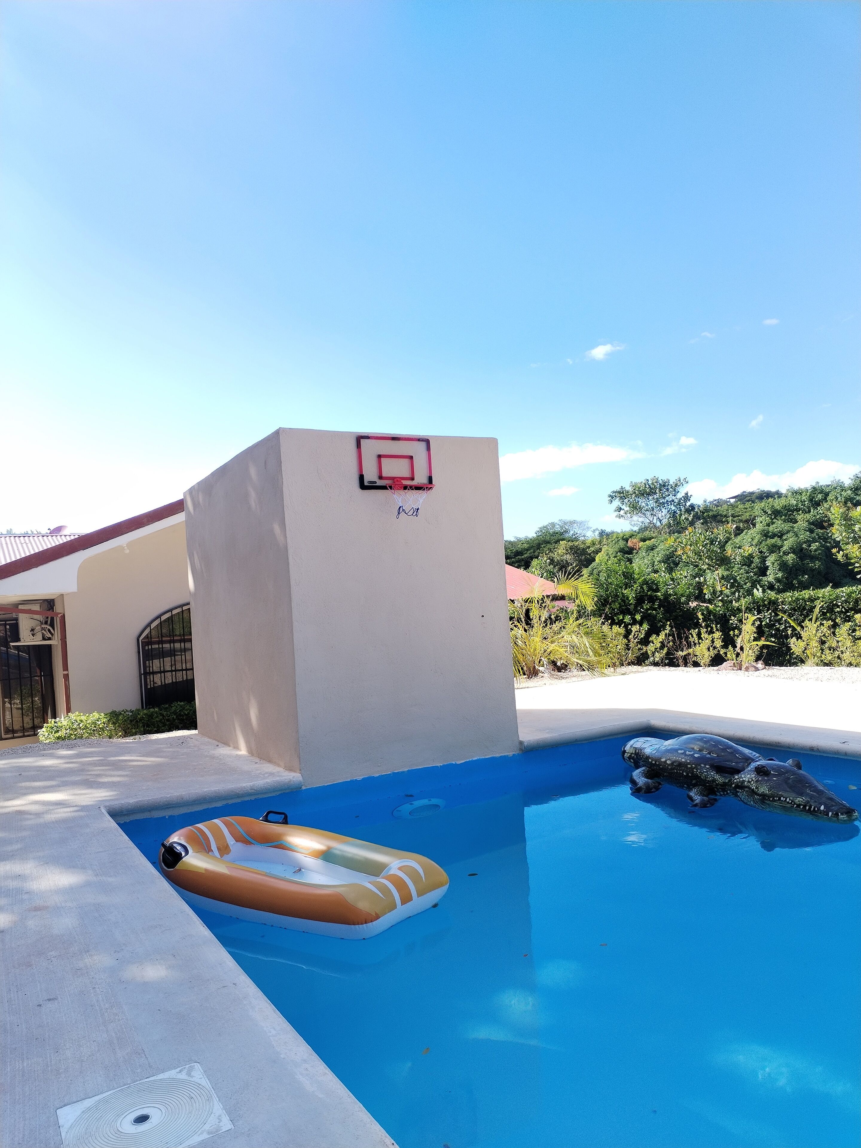 A swimming pool with a basketball hoop and a lifeguard chair.