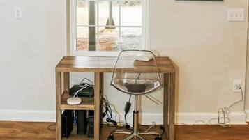 A room with a wooden desk, a chair, a window, and a framed plant.