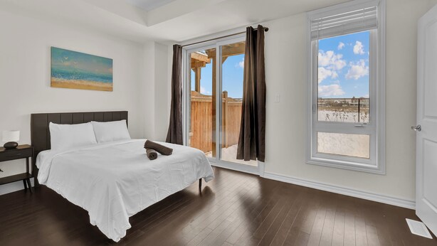 A bedroom with a large bed, a nightstand, a painting, and a view of the beach through a sliding glass door. - Embers Nest - 5 beds, 4 baths, 2 park, Backyard, Thermea Spa (Whitby)