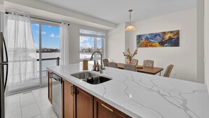 A modern kitchen with a large island, a dining area with a table and chairs, and a view of the mountains through the windows. - Embers Nest - 5 beds, 4 baths, 2 park, Backyard, Thermea Spa (Whitby)