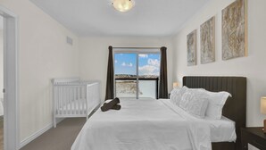 A bedroom with a large bed, a crib, and a view of the outdoors through a sliding door. - Embers Nest - 5 beds, 4 baths, 2 park, Backyard, Thermea Spa (Whitby)