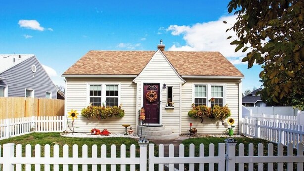 A single-story house with a white picket fence, a front porch, and a brown roof.