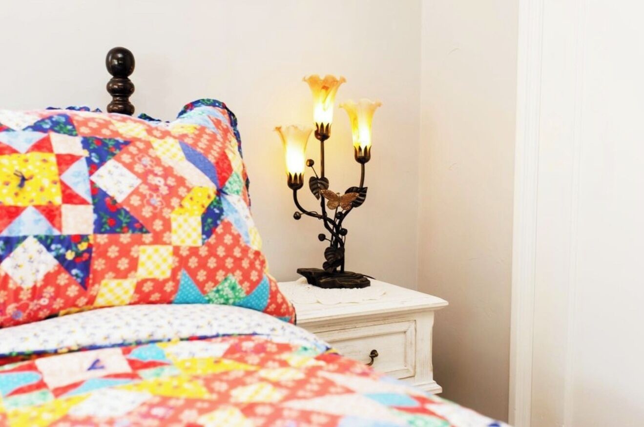 Un lit recouvert d’une courtepointe aux couleurs vives et une table de chevet blanche sur laquelle est posé un chandelier.