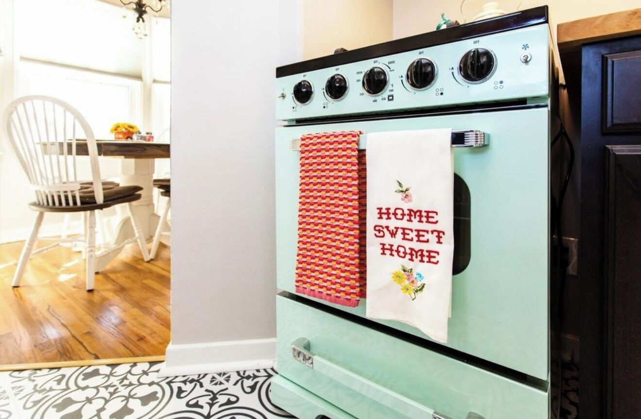 Una estufa azul vintage con una toalla roja y blanca colgada en la puerta del horno, que dice 'HOME SWEET HOME'.