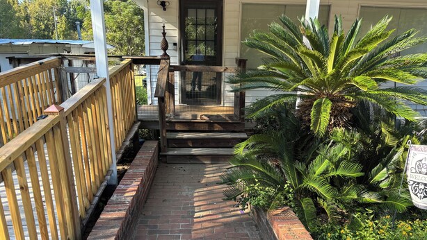 A wooden deck leading to a house with a brick pathway, a palm tree, and a welcome sign.