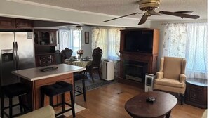 A spacious living room with a fireplace, a television, and a dining area with a kitchen in the background.