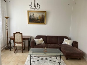 Uma sala de estar com um sofá marrom, uma mesa de centro de vidro, uma cadeira de madeira, uma mesa de jantar e um quadro na parede.
