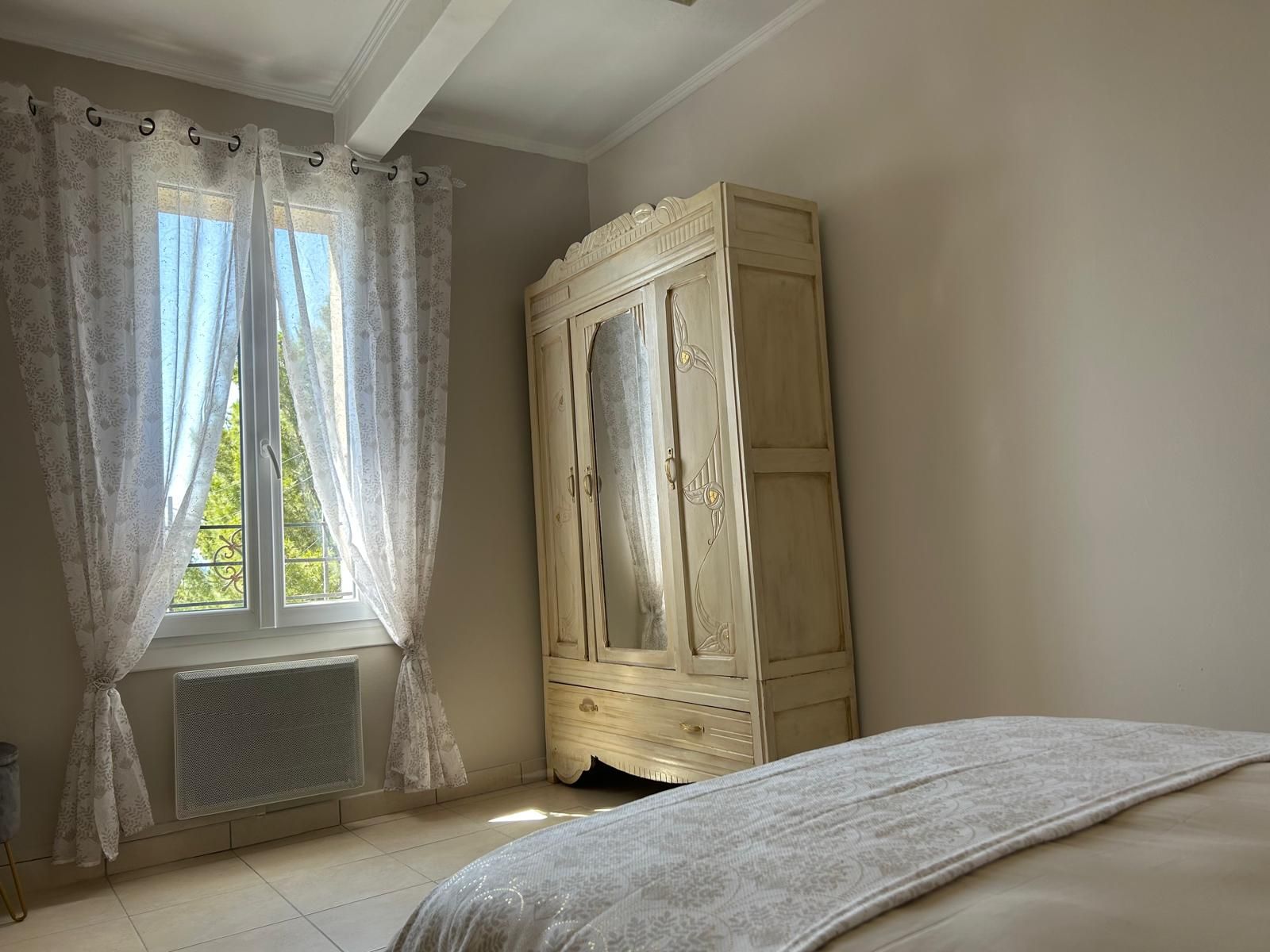 Ein Schlafzimmer mit Bett, Kleiderschrank und einem Fenster mit Vorhängen.